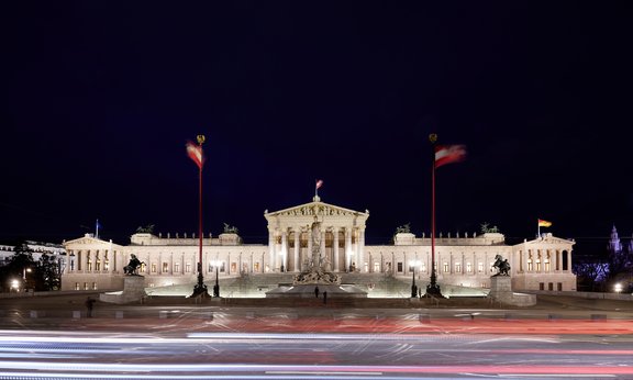 Foto Vorderansicht Parlament in Wien in der Nacht. Das Gebäude ist beleuchtet.