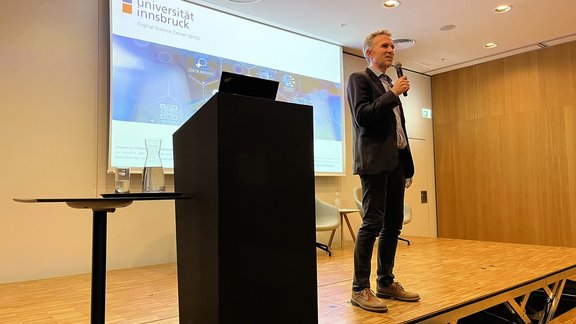 Justus Piater stands on stage, a microphone in his hand, and addresses the audience.
