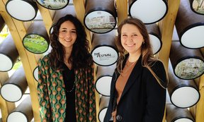 Two people stand in front of a wall with many cylindrical protrusions