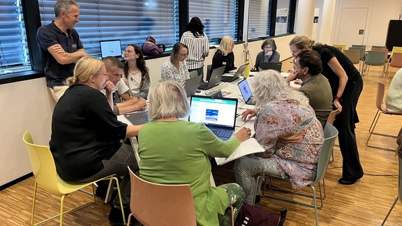 DiSCussion: How do I use AI? Participants sit at group tables in the workshop part of the event and talk to the instructors