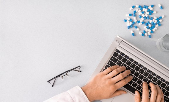 Forscher arbeitet an einem Laptop, neben ihm eine Handvoll Tabletten